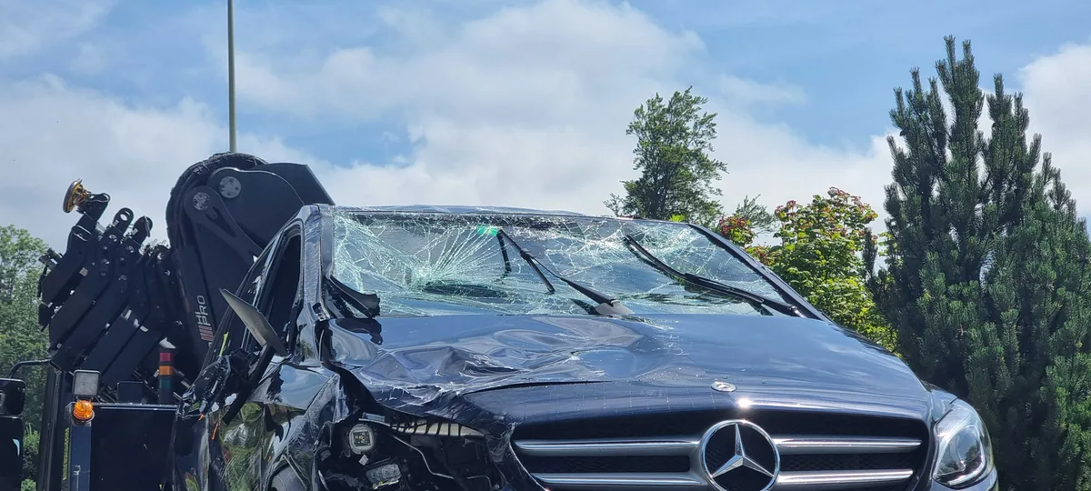 Vor allem die Beifahrerseite und die Frontscheibe vom Mercedes wurden beim Unfall beschädigt. Man sieht eine Unfallstelle und ein stark beschädigtes Unfallauto.